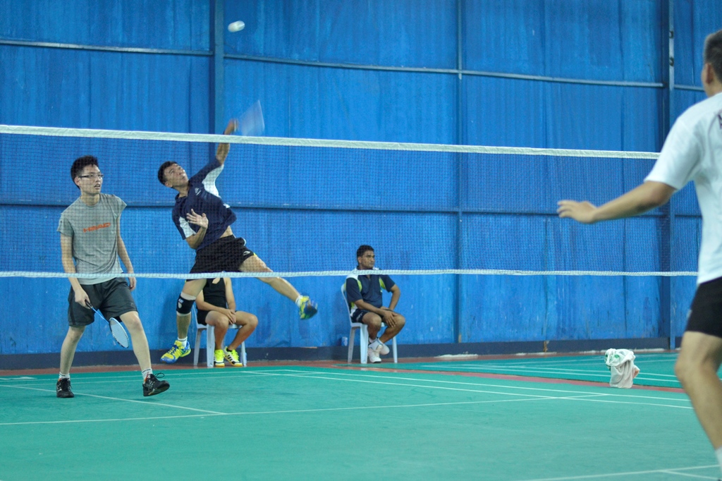 Badminton players mid-rally, one leaping for a smash